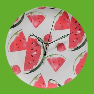 Op de afbeelding: Witte ronde klok met een watermeloen- en aardbeidesontwerp. De klok heeft zwarte wijzers en een witte achtergrond.