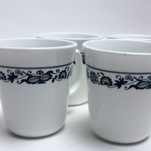 May include: Set of four white ceramic mugs with a blue floral pattern around the rim.
