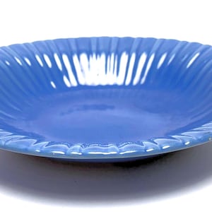 May include: A round, blue ceramic serving bowl with a wavy, ridged design around the rim. The bowl is a solid, vibrant blue color and sits on a white surface. The bowl is approximately 10 inches in diameter.