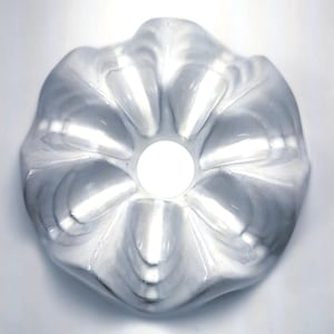 May include: A clear, flower-shaped baking mould with a central hole. The mould has a rippled design and is made of a translucent material. The overall shape is circular, with a bright white light shining through the centre.