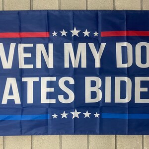 May include: A blue flag with white text that reads "Even My Dog Hates Biden". The flag has red and blue stripes with white stars.