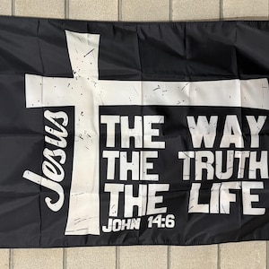 May include: Black flag with a white cross and the words "Jesus" and "THE WAY THE TRUTH THE LIFE" in white lettering. The text "JOHN 14:6" is also visible. The flag is rectangular and has a white border.