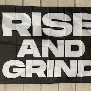 Puede incluir: Bandera negra con texto blanco que dice "RISE AND GRIND".
