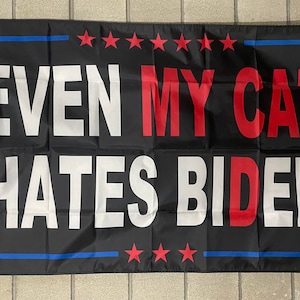 May include: Black flag with a white border and red stars. The flag says "EVEN MY CAT HATES BIDEN" in white and red letters.