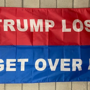May include: A red and blue flag with the text "TRUMP LOST GET OVER IT" in white letters.