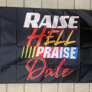Könnte beinhalten: Schwarze Flagge mit dem Text "RAISE HELL PRAISE DALE" in bunten, stilisierten Buchstaben.