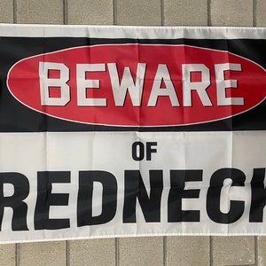 Könnte beinhalten: Eine weiße Flagge mit einem schwarzen und roten Warnschild mit der Aufschrift "BEWARE OF REDNECK".