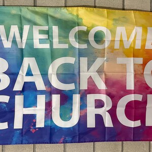 May include: A rectangular flag with the words "WELCOME BACK TO CHURCH" in large white capital letters. The background features a vibrant watercolor design with a blend of colors including blue, green, yellow, orange, and red.