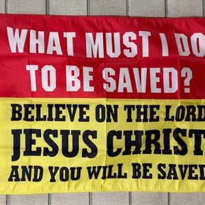 May include: A rectangular flag with a red upper half and a yellow lower half. The flag displays the text "WHAT MUST I DO TO BE SAVED?" in white, above the text "BELIEVE ON THE LORD JESUS CHRIST AND YOU WILL BE SAVED."