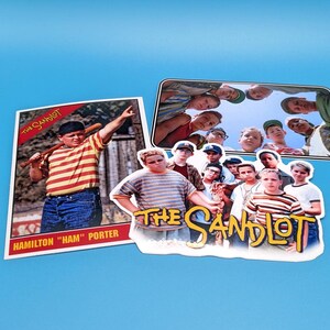 May include: A set of two The Sandlot stickers. One sticker features a baseball card of Hamilton "Ham" Porter, a character from the movie. The other sticker features a group of boys from the movie, with the text "The Sandlot" in yellow.