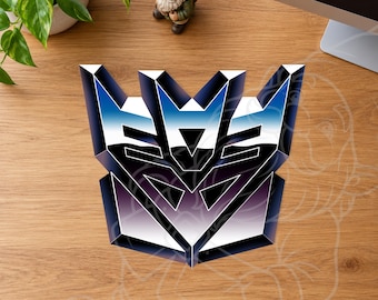 May include: A three-dimensional Decepticon logo emblem featuring a metallic gradient finish that transitions from deep blue to white and black, displaying the iconic angular robotic face design with sharp geometric edges and symmetrical shapes.