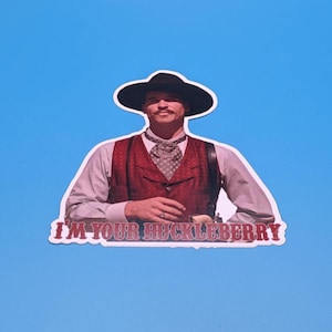 May include: A sticker featuring a man in a cowboy hat, vest, and tie, with the text "I'M YOUR HUCKLEBERRY" in red letters. The image is set against a bright blue background.