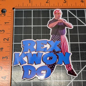 May include: A sticker featuring a cartoon image of a man wearing a red, white, and blue bandana and matching pants. The man is holding his hands in a karate pose. The text "REX KWON DO" is written in blue and red letters.