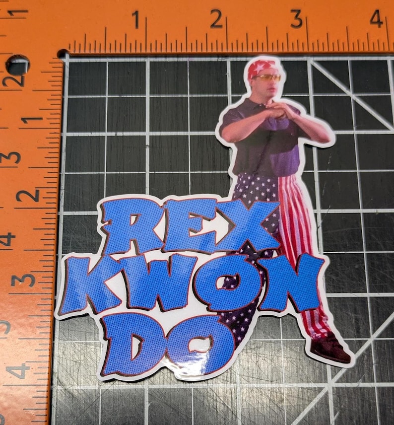 May include: A sticker featuring a cartoon image of a man wearing a red, white, and blue bandana and matching pants. The man is holding his hands in a karate pose. The text "REX KWON DO" is written in blue and red letters.
