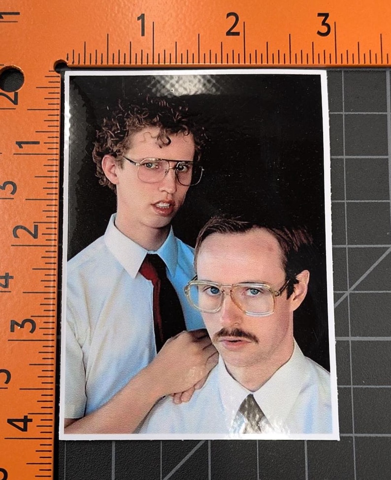 May include: Two men wearing white shirts and ties, one with curly brown hair and glasses, the other with brown hair and a mustache, are standing together. The man with curly hair is holding his hand on the other man's shoulder.