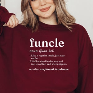 May include: A maroon sweatshirt with a white graphic print that defines the word "funcle" as a noun. The definition reads: "Like a regular uncle, just way cooler. Well trained in the arts and tactics of fun and shenanigans. See also: exceptional, handsome."