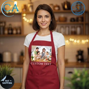 May include: A maroon apron with a large pocket and a printed image of a family cooking. The image on the apron has the text "CUSTOM TEXT" in white. The apron is worn by a person in a white t-shirt.