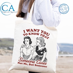 May include: Cream-colored tote bag featuring a retro illustration of two women with the text "I WANT YOU TO KNOW THAT Someone Cares Not Me, But Someone." The bag also has the "Conqueror Apparel" logo and a "Next Day Shipping" badge.