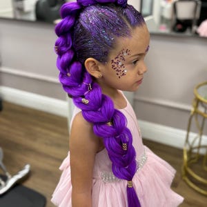 May include: A young person with vibrant purple braided hair, adorned with gold accents and glitter. The hair is styled in a side braid. The person is wearing a pink dress with a layered skirt and a jeweled belt.