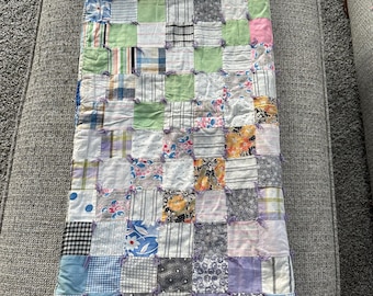 May include: A patchwork quilt featuring squares in a variety of colours and patterns, including blue, green, pink, white and black. The quilt is made from different fabrics and has a rustic, vintage feel.