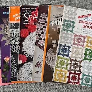 Op de afbeelding: Een verzameling vintage haakpatroonboeken, met kleurrijke covers met bloemen- en geometrische ontwerpen. De boeken bevatten titels als "SPA Crocheted" en "The Famous Puritan Crochet Book". De covers tonen verschillende kleuren, waaronder rood, paars en geel.