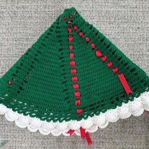 May include: A handmade, green crocheted Christmas tree skirt with a scalloped white border. Red ribbon accents are woven through the green crochet, adding a festive touch. The tree skirt is triangular in shape.