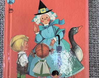 May include: A vintage Mother Goose Tip-Top Elf book with a coral-orange cover. The illustration features a woman in a blue dress and black witch hat, a goose, and two children. Text includes MOTHER GOOSE, 29 cents, 8647, and A RAND MCNALLY BOOK.