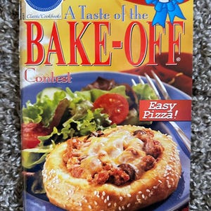 May include: A Pillsbury Classic Cookbooks softcover book titled A Taste of the BAKE-OFF Contest. The cover features a blue plate with a Double Cheeseburger Pizza Round and a side salad, with text highlighting winning recipes and Easy Pizza.