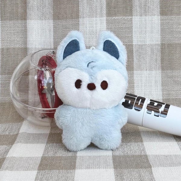 May include: A light blue plush fox with dark blue ears and brown eyes. The fox is holding a white and silver light stick with the text "GO RJ" printed on it.
