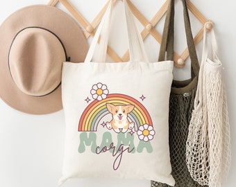 May include: A white tote bag with a rainbow, flowers, and a cartoon corgi dog. The text "Mama Corgi" is printed on the bag.