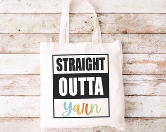 May include: A white tote bag with black text that reads "STRAIGHT OUTTA yarn" in a black box with a colourful "yarn" underneath.