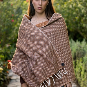 May include: A brown and white patterned shawl with fringe. The shawl is draped over a person's shoulders and is worn with blue jeans.