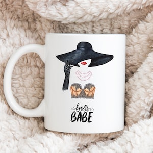May include: White ceramic mug with a black and white illustration of a woman wearing a black hat and a lace bra. The text "boss babe" is written in black cursive below the illustration.