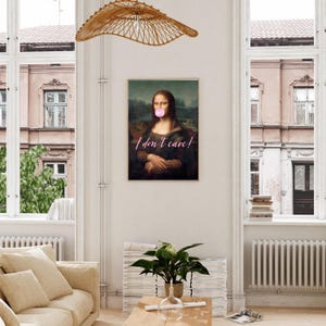 May include: A framed print of the Mona Lisa with a pink bubble gum in her mouth. The text "I don't care!" is written in pink below her. The print is hanging on a white wall in a room with a couch and a plant.