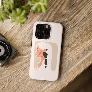 Op de afbeelding: Witte telefoonhoes met een minimalistische illustratie van een vrouwenprofiel. De illustratie is in tinten bruin, zwart en wit.