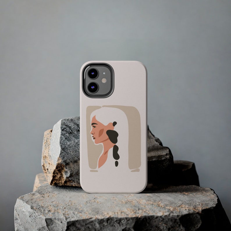 Op de afbeelding: Een witte telefoonhoes met een minimalistisch ontwerp met een vrouwenprofiel in zwart en bruine tinten. De hoes heeft een uitsparing voor de cameralens en een neutrale achtergrond.