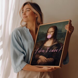 May include: A framed print of the Mona Lisa with a pink bubble gum added to her mouth. The print has the text "I don't care!" written in pink cursive.