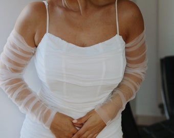 May include: A white dress with a fitted bodice and a flowing skirt. The dress has sheer, long sleeves and a scoop neckline.