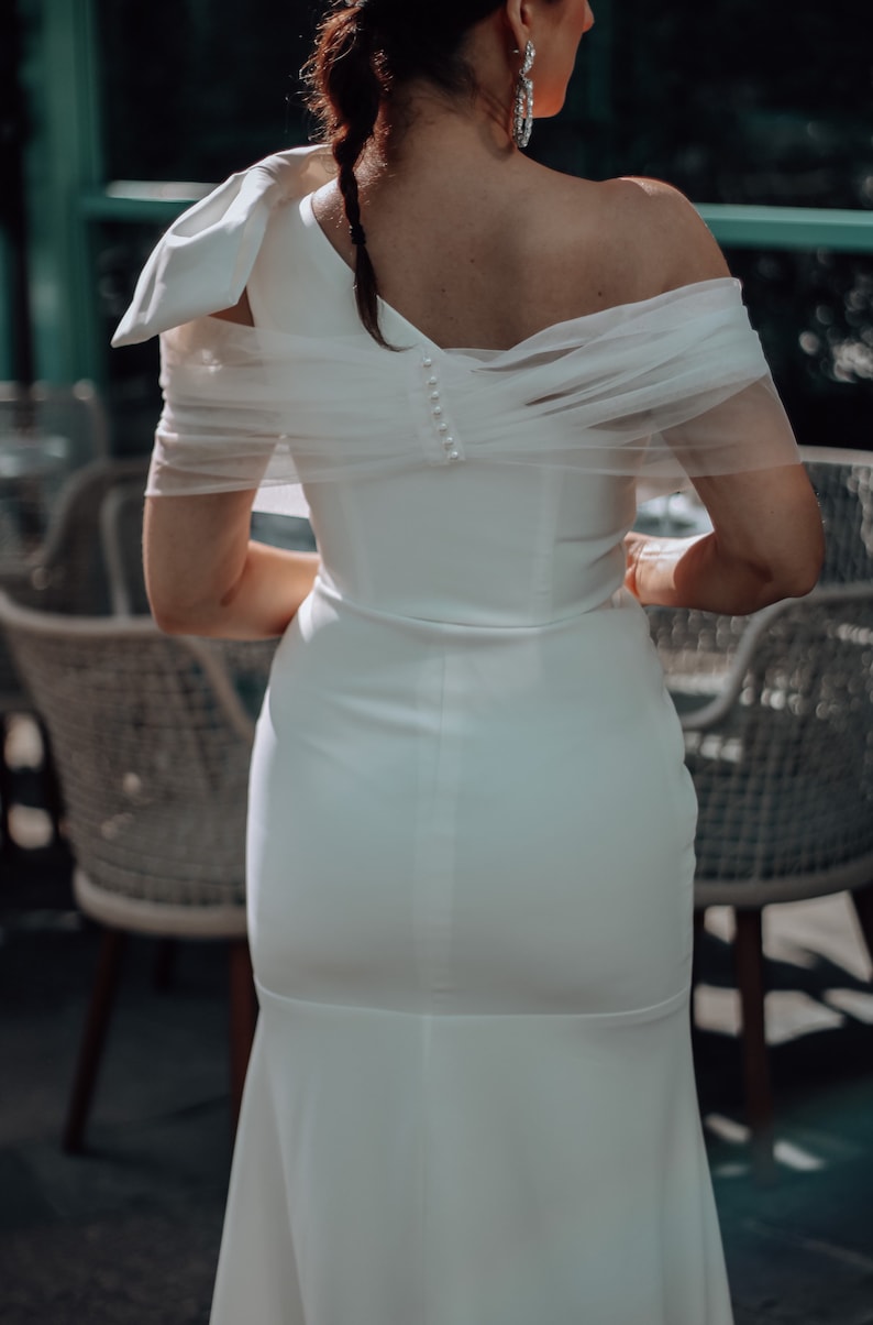 May include: A white off-the-shoulder wedding dress with a tulle overlay and a fitted skirt.