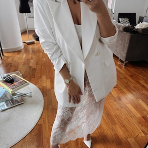 May include: A white blazer with pearl buttons and a white lace skirt.