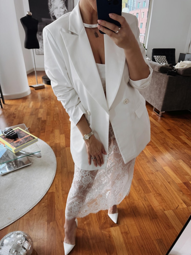 May include: A white blazer with pearl buttons and a white lace skirt.