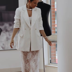 May include: A white blazer with a double breasted closure and a white lace skirt.