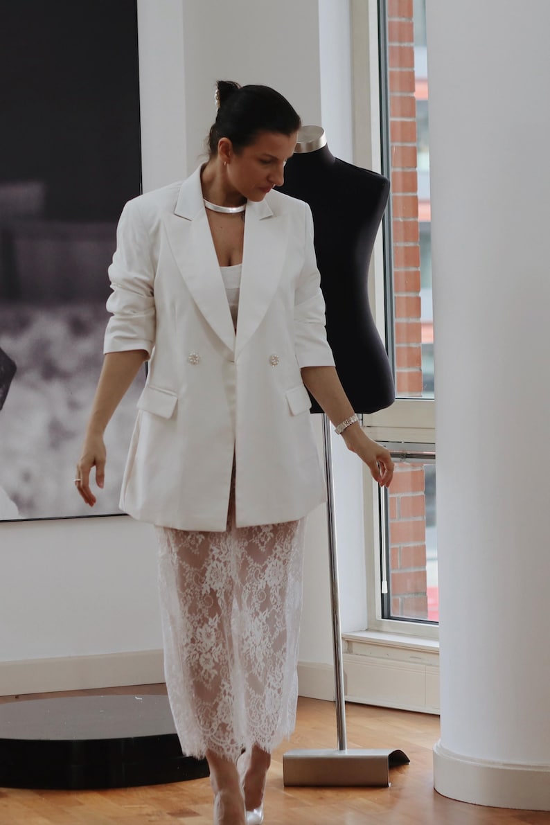 May include: A white blazer with a double breasted closure and a white lace skirt.