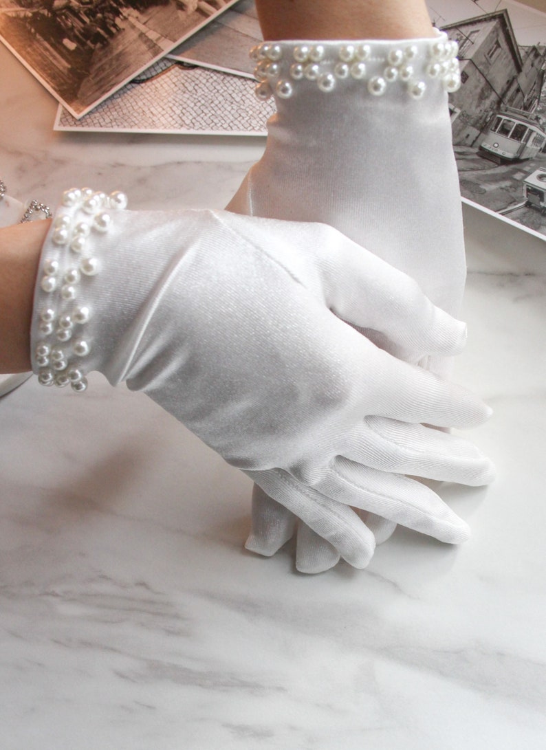 May include: A pair of white satin gloves with pearl embellishments at the wrist.