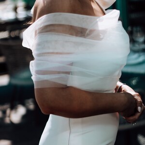 May include: A white off-the-shoulder dress with a sheer overlay and a fitted silhouette.