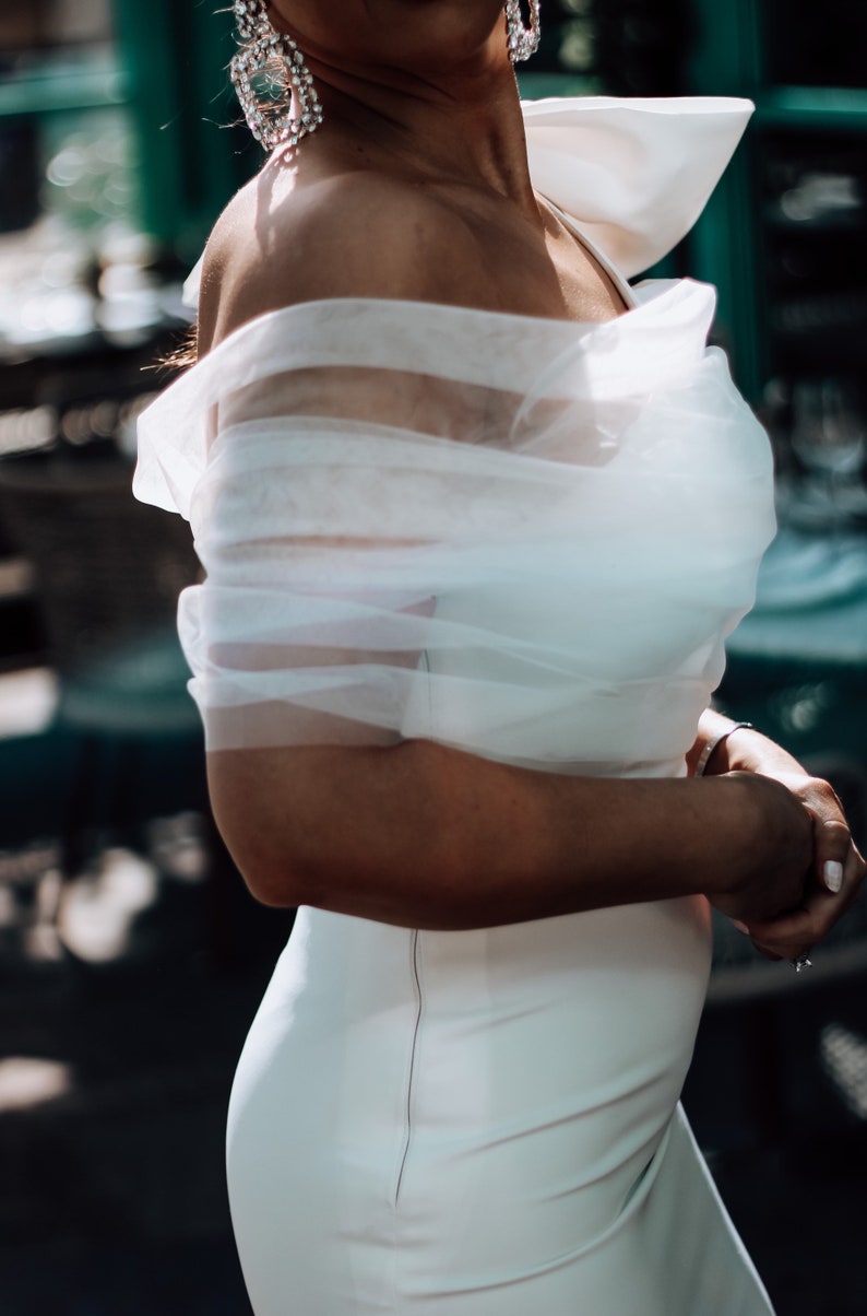 May include: A white off-the-shoulder dress with a sheer overlay and a fitted silhouette.