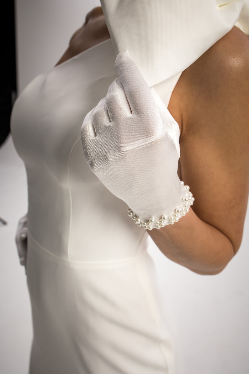 May include: A white satin glove with a pearl bracelet on the wrist.