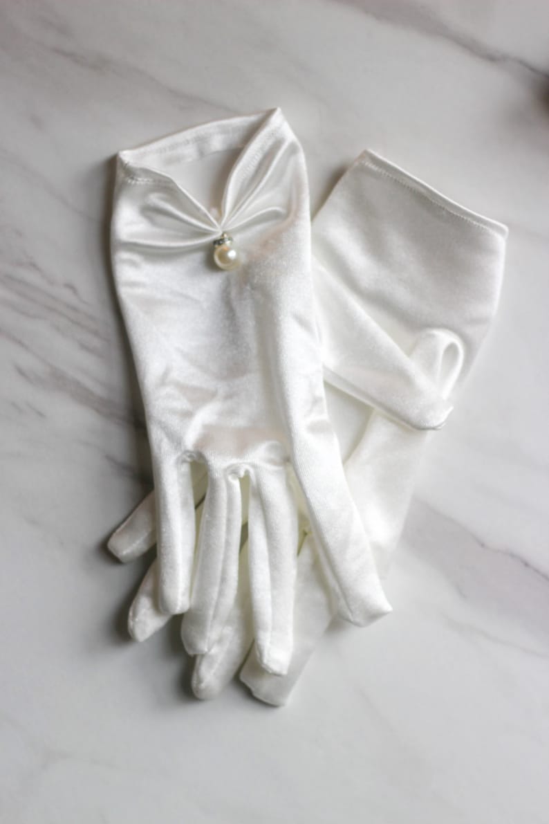 May include: A pair of white satin gloves with a pearl embellishment on the back of the hand.