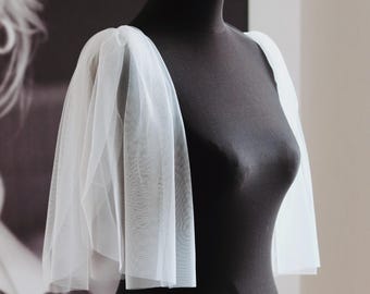 May include: White tulle fabric sleeves for a wedding dress or other formal attire. The sleeves are gathered at the shoulder and have a flowing, romantic look.