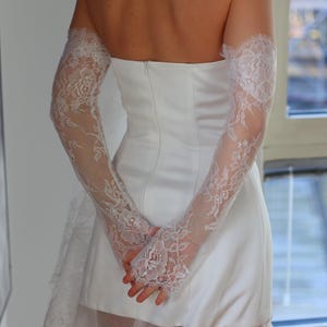 May include: A white strapless wedding dress with a lace overlay and long lace sleeves. The dress has a fitted bodice and a flowing skirt.